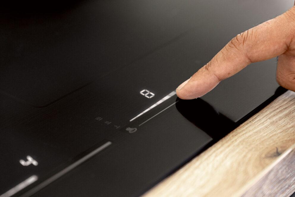 Nahaufnahme einer Hand bei der Touch-Bedienung des leuchtenden Flex-Sliders auf einem benthaus Induktionskochfeld für direkte Temperatursteuerung.